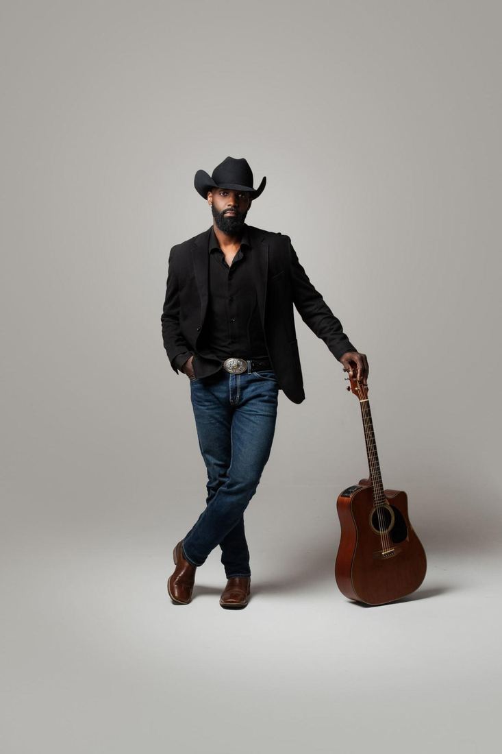 Jesse Daniels standing in a black blazer with an acoustic guitar