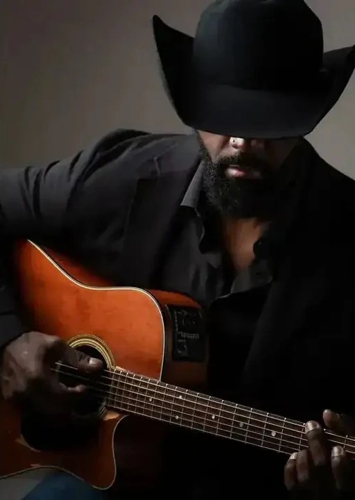 Country artist Jesse Daniels playing acoustic guitar in a black cowboy hat