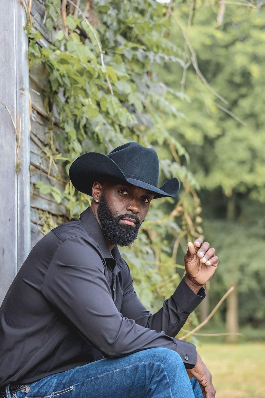 Jesse Daniels in a black cowboy hat and dark shirt, seated on a weathered porch