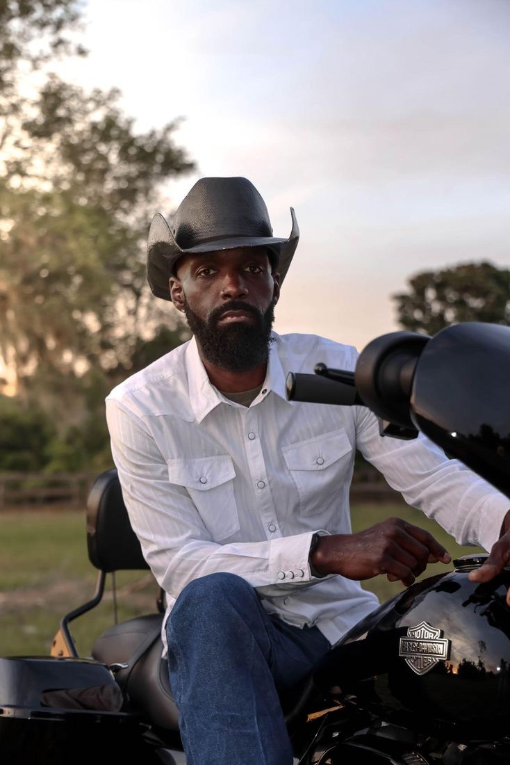 Jesse Daniels in a cowboy hat and white western shirt on a motorcycle at sunset